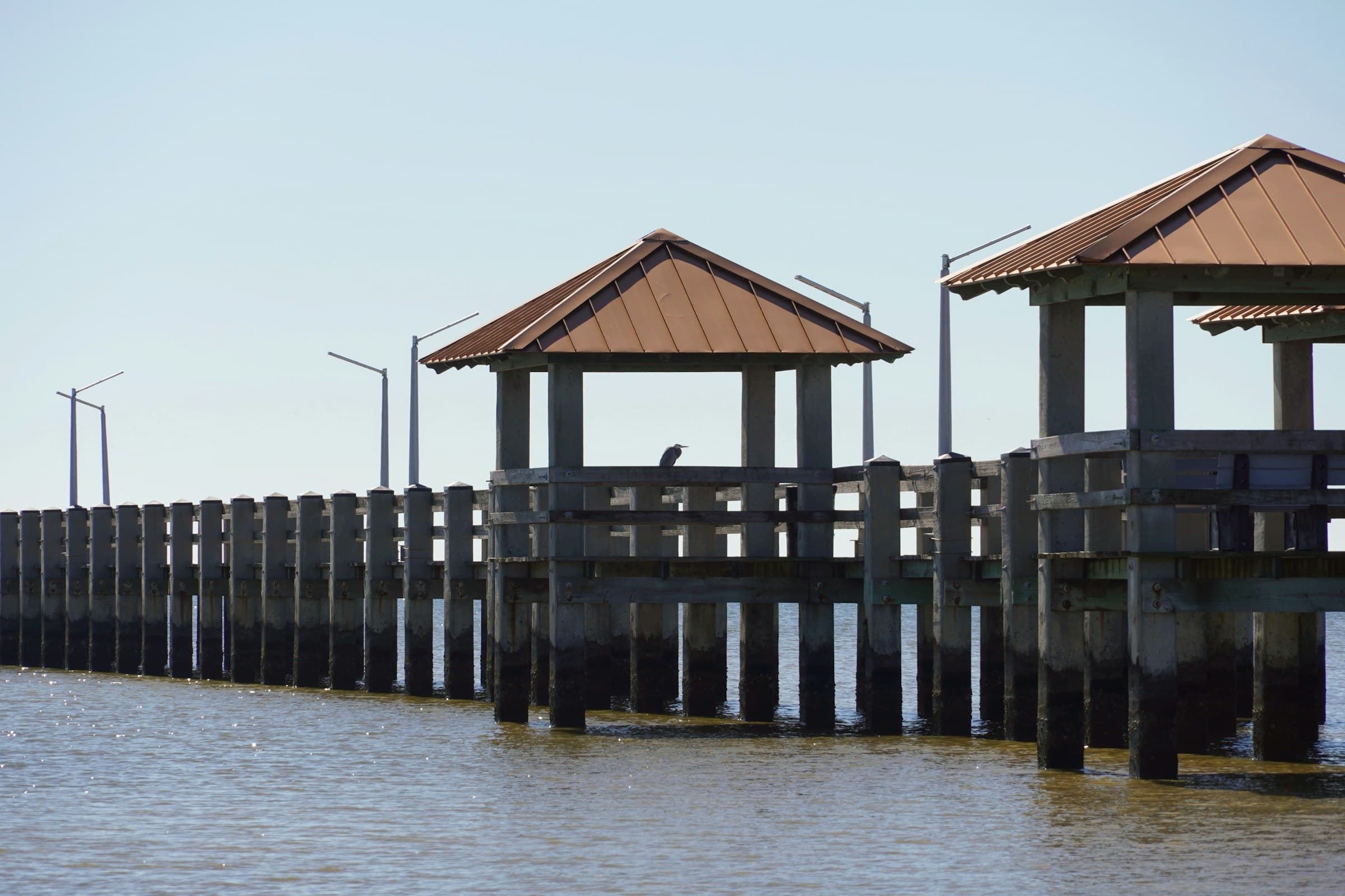 A timber fishing pier on standing piles reaching out over coastal water.