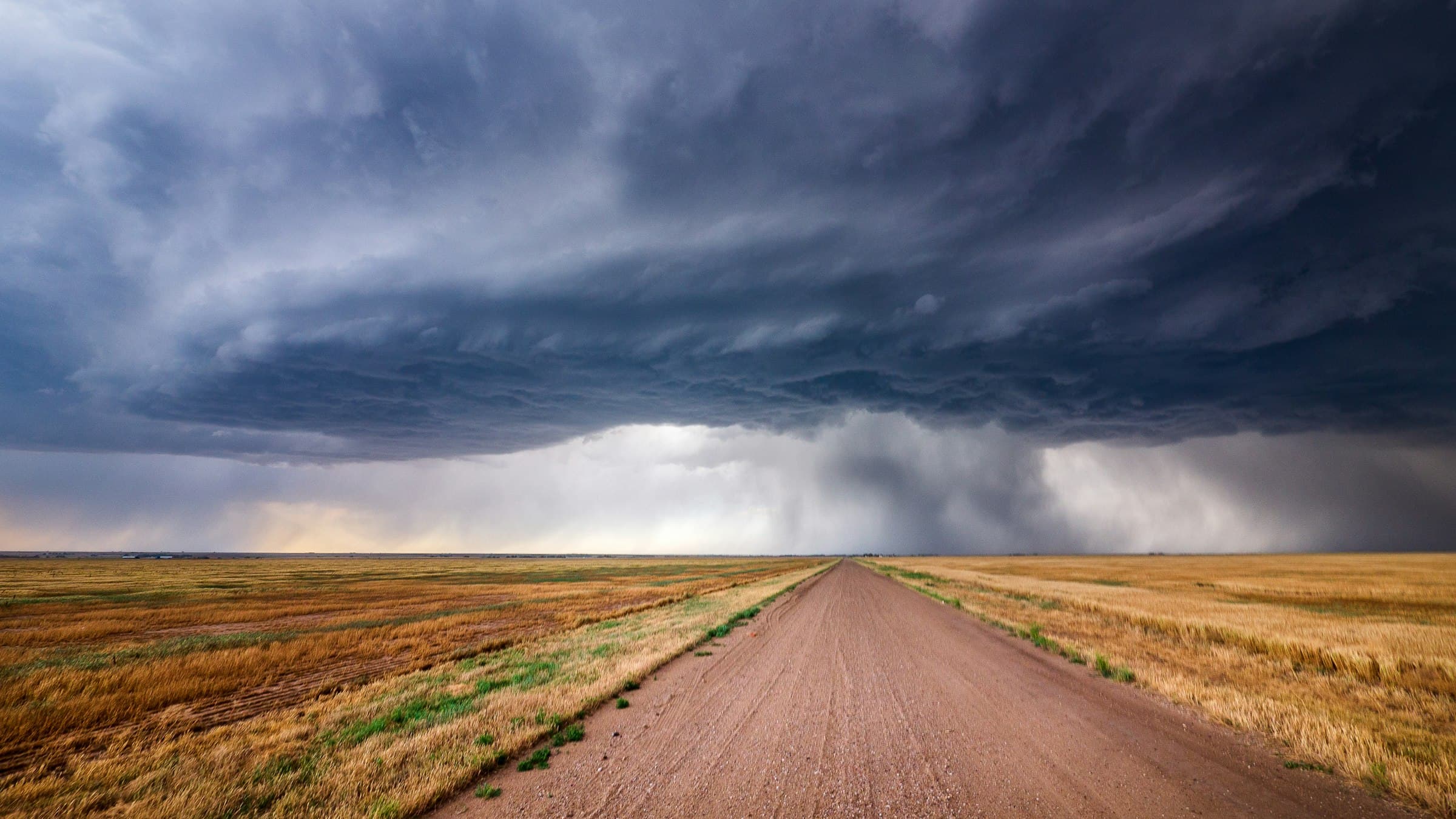 A dirt road running straight across open country under grey cloud.
